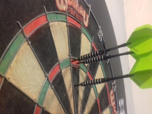 Dart board with three green darts Gors-lŵyd Games Room